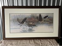Framed numbered print 'Winging Westward' showing Canada geese flying over water in a natural setting, mounted with mat and wood frame.