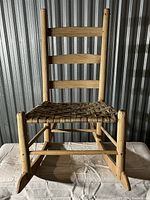 Front view of child size wooden rocking chair showing ladder back design and woven reed seat.