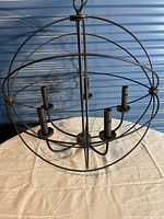 Full view of round cage pendant light fixture with 5 bulb holders arranged inside spherical metal cage structure on a surface.