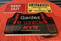 Three signs displayed on a red blanket: KYB illuminated sign with wiring, Keep Out reflective sign, Caution Construction in Progress sign.