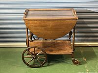 Full side view of the tea cart showing wooden spoked wheels, bottom shelf, and drop leaves in folded position.