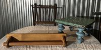 Three vintage home objects on a table, including a hanging magazine rack, a towel bar, and a footstool