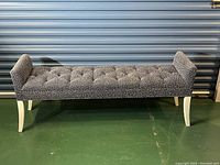 Front angle view of upholstered bench showing tufted seat and curved white legs with armrests at each side.