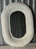 Front view of an oval mirror with a white painted woven wicker frame showing textured wicker craftsmanship and glass mirror surface.