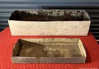 Front view showing large and medium metal planter box inserts positioned one behind the other on a red surface.