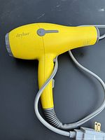 Photo of yellow Drybar hair blow dryer showing full side profile and attached power cord with plug.