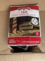 Photo of a partially open box showing 'Holiday Time 150 Clear Ribbon Net Lights' branding and product image of ribbon net lights wrapped around a tree trunk.