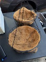 Top and side view of the three-tier hanging kitchen fruit basket showing black metal wire construction and coconut fiber liners.
