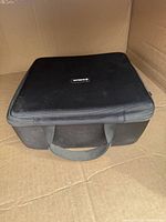 Closed black zippered hard case for drill with handle visible on front.