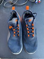 Full view of the top of the Nike shoes showing black mesh fabric, orange details, black laces, and white sole.