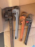 Four pipe wrenches in a box of varied sizes and colors.