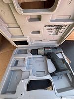 Ryobi cordless drill inside the molded plastic carrying case showing sections for bits and storage, drill placed on the right side with some dust and wear on case.