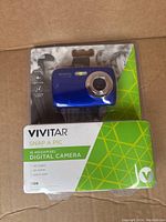 Front view of Vivitar Snap A Pic S126 digital camera in retail packaging showing the blue camera through clear plastic with product details on cardboard backing.
