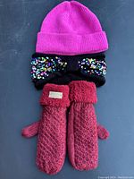 Photo showing pink ribbed knit hat with black sequin bow and pair of red mittens with faux fur cuffs.