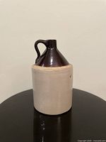 Front view of ceramic whiskey jug with beige base and dark brown conical neck and handle.