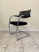 Side profile of the Vitra Visasoft Visavis cantilever chair showing black perforated backrest, chrome frame and black upholstered seat