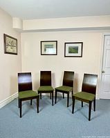 Four modern dining chairs with dark wood frames and green seats against a light wall in a room with carpet.