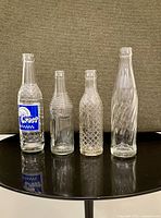 Four vintage glass soda bottles arranged side by side showing label and embossing details