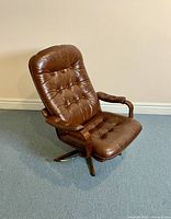 Front-angle view capturing the brown leather seat and backrest with button tufting, curved plywood armrests, and dark faux rosewood swivel base.