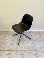 Front angle view of the charcoal grey modern swivel chair by Muuto, showing smooth plastic seat and metal swivel base.