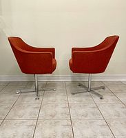 Side profile of two mid-century swivel armchairs showing curved backs and armrests in burnt orange fabric with chrome bases on tiled floor.