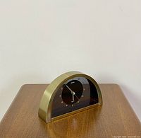 Side angle view of semi-circular Seiko clock showing brass finish and black clock face with gold-tone markers and hands