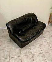 Front and side angled view of black vinyl loveseat showing overall condition and design.