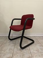 Right front angled view showing burgundy upholstered seat and backrest with black tubular metal armrests and cantilever base.