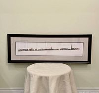 Full view of the framed horizontal print hanging on a wall above a round covered table.