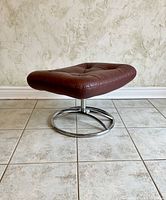 Front-left angle view of ottoman showing tufted leather top and circular chrome base