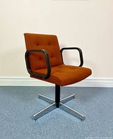 Front view of vintage burnt orange swivel office chair with black loop armrests and chrome base