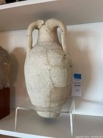 Frontal image of the amphora on an acrylic stand, showing the shape, handles, and patched repairs on the surface.