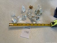 Wide shot showing all seven glass figurines arranged on a textured light surface with measurement tape indicating size around 3 inches or less