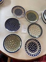 Top view of six assorted Polish pottery plates displaying diverse hand-painted patterns with circles, dots, and floral motifs in blue, yellow, green, and white.