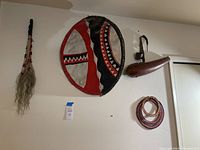 Full view of all items hanging on the wall: shield, fly swatter, milk gourd, beaded necklaces