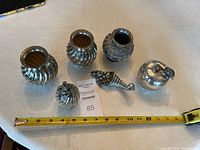 Overview of all six silver-toned decorative items on table with tape measure showing sizes