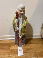 Full view of the Chinese porcelain statue of Shouxing standing approximately 18 inches tall, showing the figure holding a red staff and wearing a yellow patterned robe.