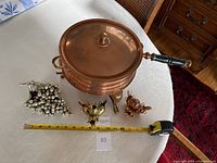Wide shot of vintage copper chafing dish with lid, two bird-shaped toothpick holders, and silver-tone metal grape bunch decoration, with tape measure showing approximately 13 inches length.