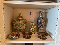 Wide view of porcelain urn, vase, small jar, brass candle holders and glass candy dish on shelf