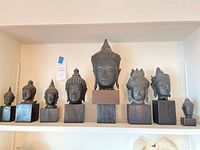 Full front view of eight metal Buddha head sculptures on wooden bases arranged on shelf