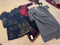 Three garments on carpet including black and red embroidered dress, black and gold two-piece outfit, and gray long wool coat.