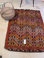 Photo showing the vintage kilim rug with geometric patterns in multiple colors and the round woven basket beside it on a carpeted floor.