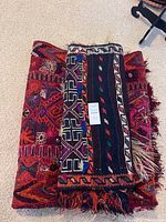 Two flat weave floor coverings folded and stacked, showing color and fringe condition