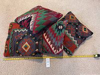 Four kilim style pillows arranged on carpet with measuring tape showing approximately 19 inches square each