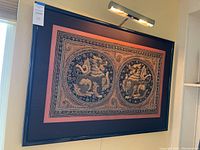 Full view of framed Kalaga embroidery hung on wall with picture light above