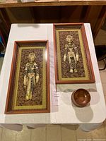 Overview showing two framed shadow box vintage Chinese coin dolls on cork background, plus two small copper bowls on white table.