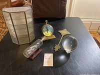 Photo showing the entire lot including round glass clock/compass, ship in bottle on stand, brass Ethiopian cross, glass sphere, and the hanging glass cabinet in the background