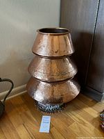 Side view of three copper containers stacked on beaded stand, showing hammered texture and tapered shapes.