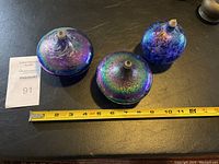 Three iridescent art glass oil lamps arranged side by side with measuring tape to show size.
