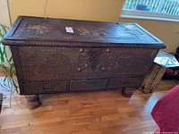 Front view of chest showing hinged lid, brass stud decoration, front drawers and turned wood legs